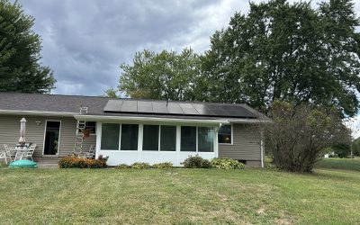 Suburban house with rooftop solar panels, a person at the doorway, patio furniture, ladder and cloudy sky