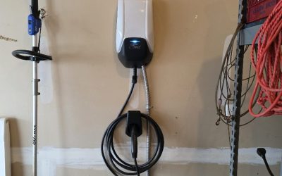 Ford EV wall charger mounted in garage, coiled charging cable with nearby shelving, cords and garden tools