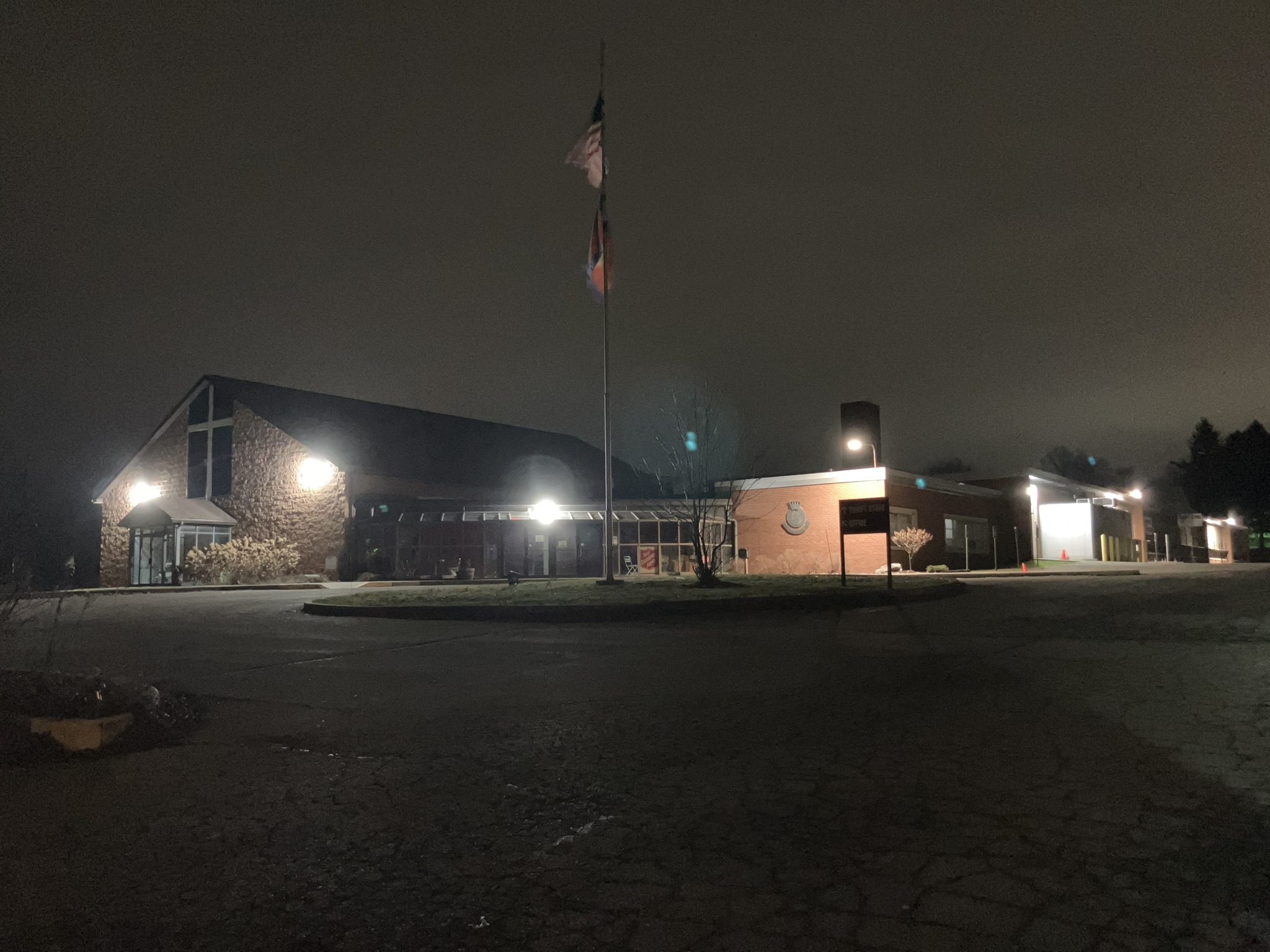 Lit brick building at night with central flagpole, illuminated entrances and empty parking area