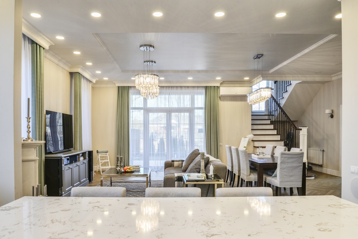Open-plan living and dining room with marble island, crystal chandeliers, sofa, dining table and staircase