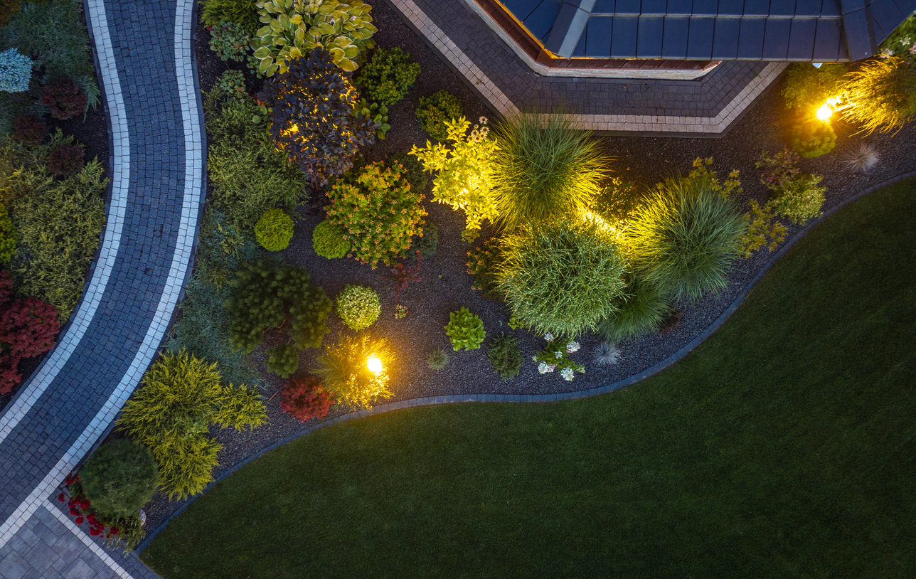 Aerial view of illuminated landscaped garden with curved stone walkway and manicured lawn at dusk