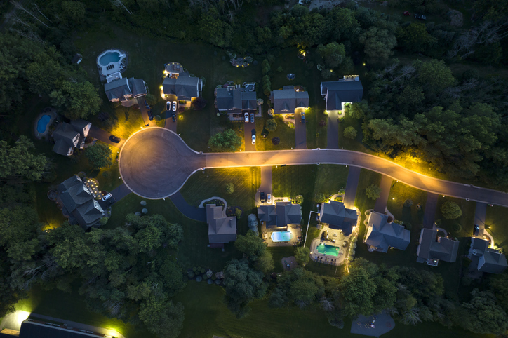 Aerial nighttime view of illuminated suburban cul-de-sac with houses, swimming pools and tree-lined streets.