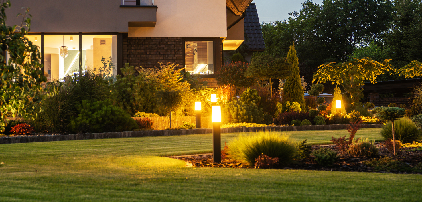 Modern house at dusk with glowing pathway lights and a manicured landscaped front yard.