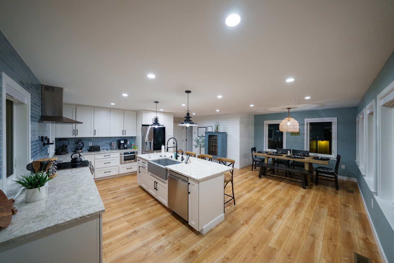 Open-concept modern kitchen with large island, pendant lights, white cabinets, blue accent wall and adjacent dining area