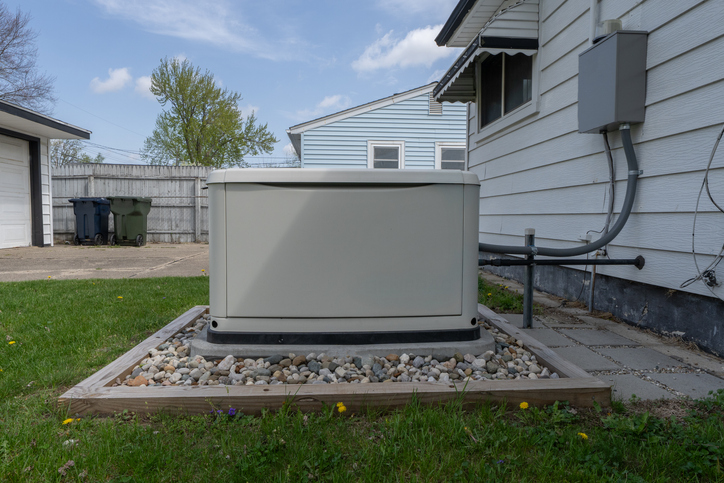 Residential standby generator on rock bed beside house with electrical conduit and lawn