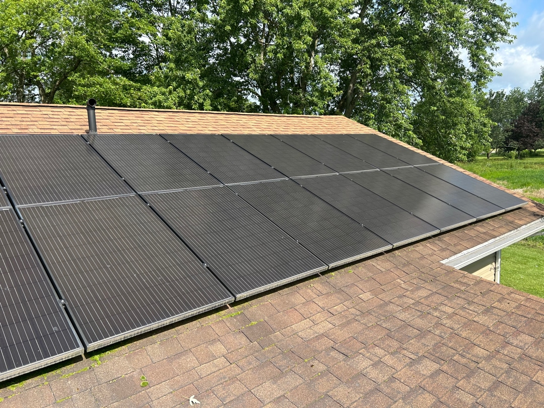 Residential rooftop solar panel array on asphalt shingle roof with trees and blue sky